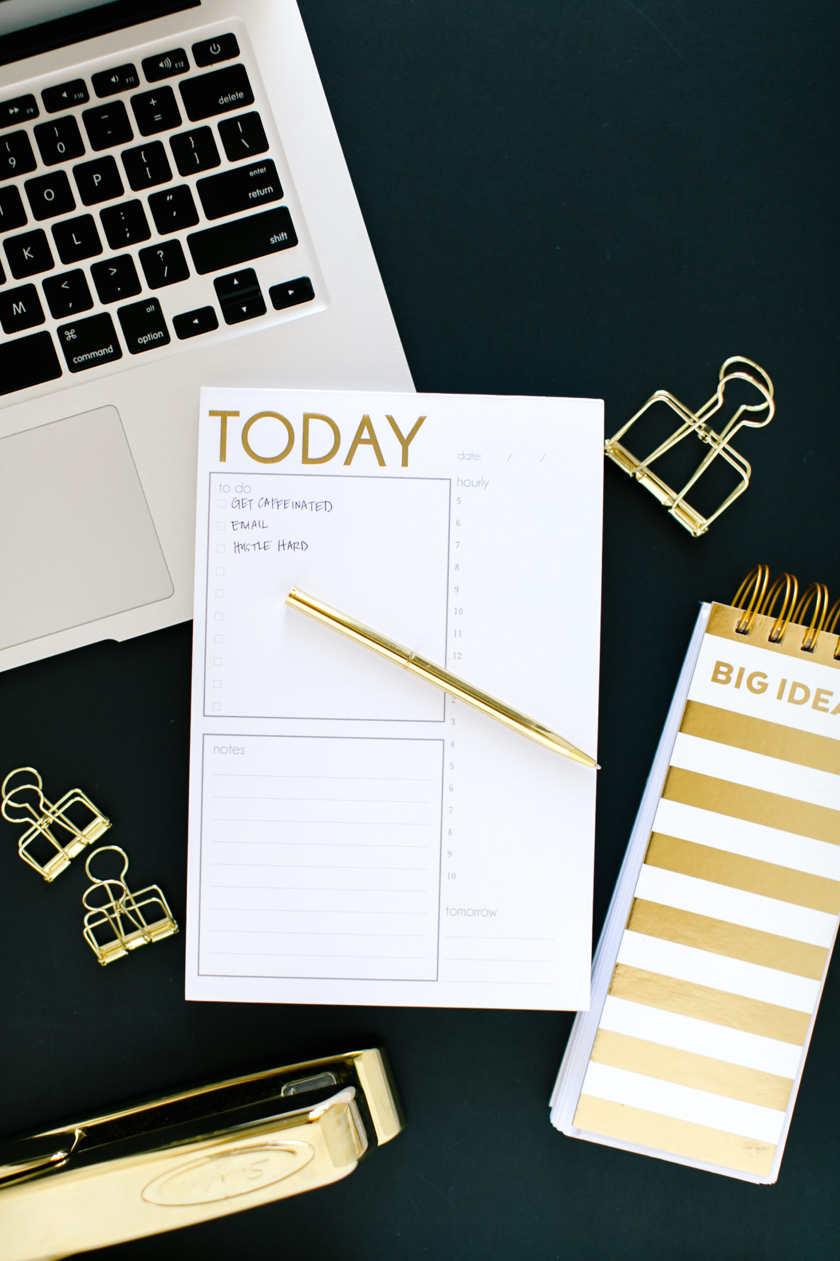 A tabletop with an open laptop, a cup of coffee, a notepad and pen, and a cell phone.