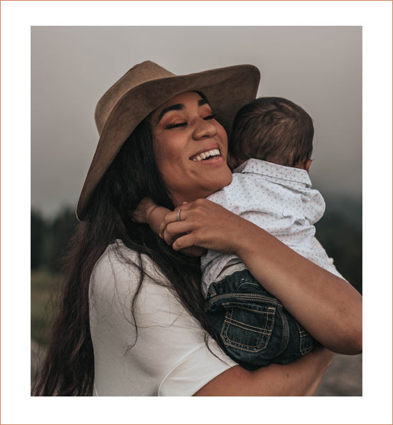 A black mother holding her baby in a hug with a big smile on her face.